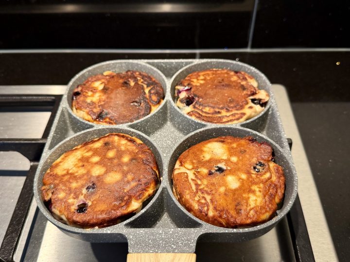 Blueberry banana protein pancakes frying in a pancake pan with coconut oil